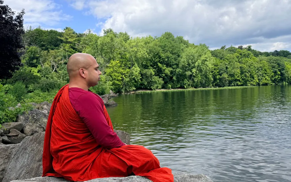 Buddhist monk meditating beside a peaceful lake surrounded by nature